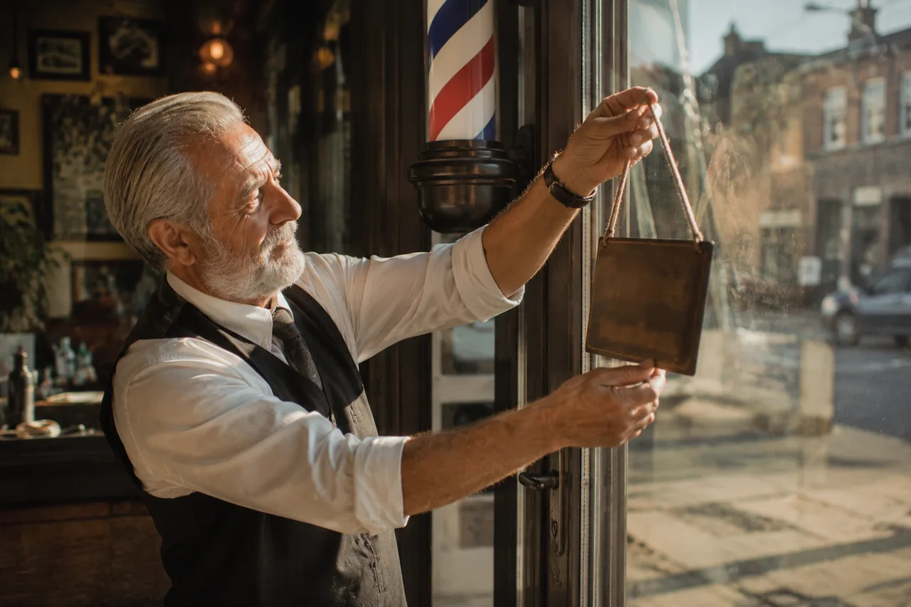 A barber hanging the sign on his shop's glass door in early morning light